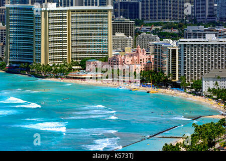 La spiaggia di Waikiki con costa e alberghi in background. edificio rosa, alberghi, barche a vela catamarano, nuotatori e surfisti Foto Stock