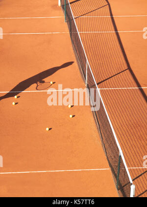 Ombra del giocatore di tennis a net con scatttered le palline da tennis su clay court Foto Stock