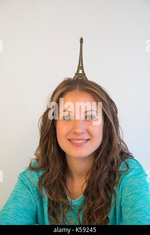 Giovane donna sorridente con una riproduzione in scala della torre Eiffel sul suo capo. Foto Stock