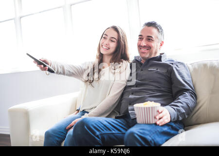 Ritratto di un giovane uomo e la figlia di guardare la tv mentre mangiare popcorn sul divano Foto Stock