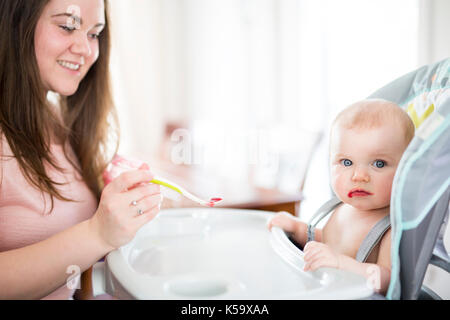 Alimentazione madre bambina in sedia alta Foto Stock