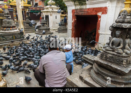 Un giovane ragazzo con suo padre alimenta i piccioni intorno al kathesimbhu shree gha stupa di Kathmandu, Nepal. Foto Stock