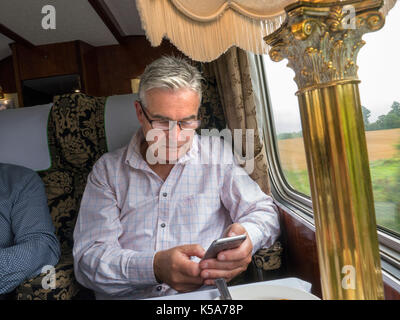 Treno di lusso Travel imprenditore texting sul suo smartphone iPhone mentre la finestra seduto in una prima classe Pullman di lusso carrozza ferroviaria treno Foto Stock