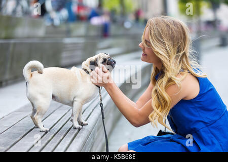 Giovane donna accarezza un pug che si siede su un banco di lavoro Foto Stock