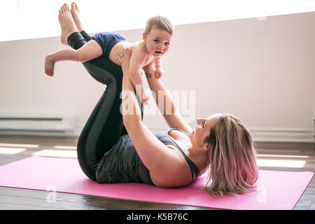 Giovane madre non fisico esercizi di yoga insieme con il suo bambino Foto Stock