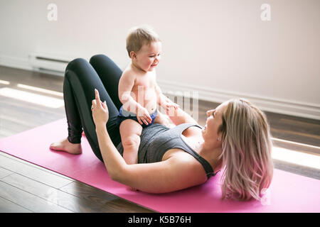 Giovane madre non fisico esercizi di yoga insieme con il suo bambino Foto Stock