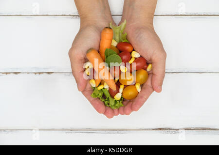 Donna che mantiene molti vegetali nelle mani di bianco su un tavolo di legno. Foto Stock
