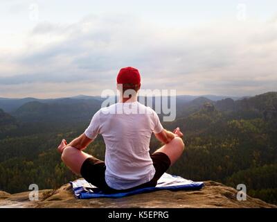 Solo l'uomo seduto a praticare yoga pone su uno sperone roccioso a picco. L'uomo all'interno di foschia mattutina fare meditazione e gode di vista valle Foto Stock