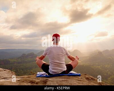 Solo l'uomo seduto a praticare yoga pone su uno sperone roccioso a picco. L'uomo all'interno di foschia mattutina fare meditazione e gode di vista valle Foto Stock