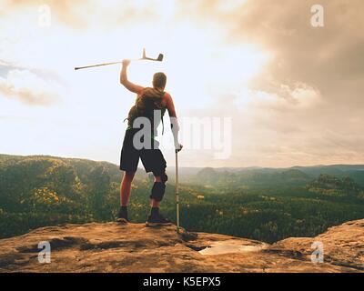 Uomo con le stampelle e la gamba rotta fissata in ortesi per ginocchio caratteristica.traveler con gamba ferito in bendaggi soggiorno sul roccioso punto di vista nelle montagne. escursionista con Foto Stock