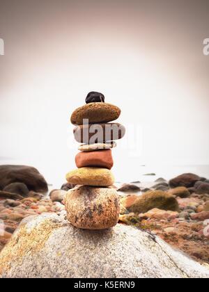 Piramide di pietre che simboleggia lo zen, armonia, equilibrio ciottoli. oceano in background. colorato pietre piatte per la meditazione giacente su terreni sassosi mare spiaggia Foto Stock