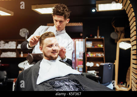 Il barbiere uomo nel processo di taglio della barba di client tosatrici elettriche Foto Stock