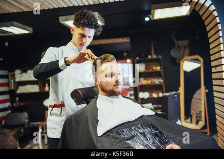 Il barbiere uomo nel processo di taglio della barba di client tosatrici elettriche Foto Stock