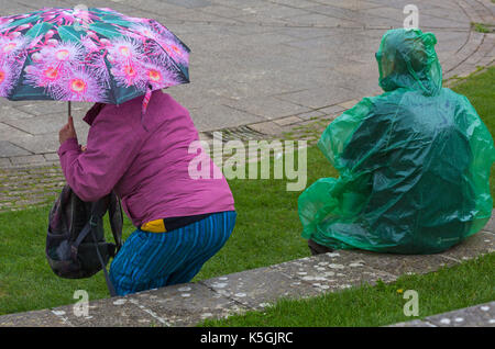 Swanage, Dorset, Regno Unito. 9 Sep, 2017. Regno Unito meteo: heavy rain e tuoni a Swanage. Uomo seduto sulla parete in verde poncho impermeabile e la donna con ombrello. Credito: Carolyn Jenkins/Alamy Live News Foto Stock