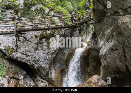 Giovane donna attraversando un ponte di legno su una cascata Foto Stock