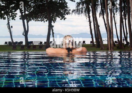 Donna in piscina in Thailandia guardando il mare.donna rilassante vicino alla spiaggia in krabi.bianco plumeria fiore su una donna capelli.Mare delle Andamane Foto Stock