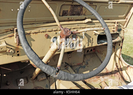 Jeep militare d'epoca con cabina anteriore aperta, cruscotto e volante che mostrano la ruggine degli elementi. Foto Stock