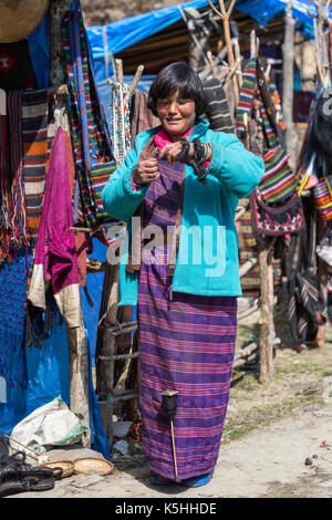 Signora la filatura yak capelli mentre tendendo artigianato e souvenir si erge a pele la mountain pass, centrale bhutan Foto Stock