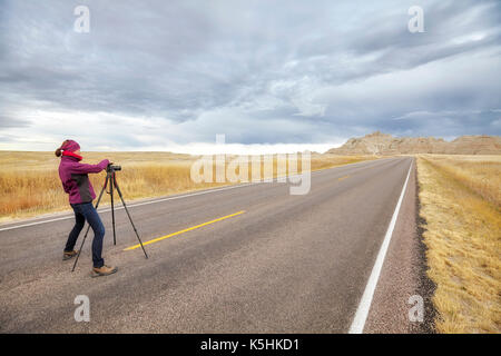 Fotografo di paesaggio prende le immagini su una strada vuota con cielo tempestoso, di viaggio o di lavoro concetto, Parco nazionale Badlands, Dakota del Sud, Stati Uniti d'America. Foto Stock