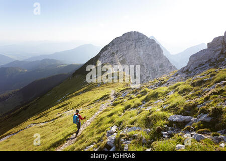 Donna con zaino blu scendendo ripida Kladivo montaggio in una bella giornata di sole, Karavanke, Slovenia. Foto Stock