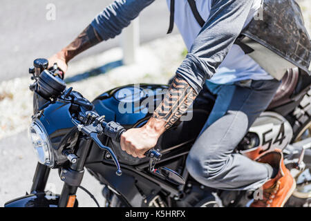 Fresco guardando i tatuaggi sui bracci del motociclista su custom made stile scrambler cafe racer Foto Stock