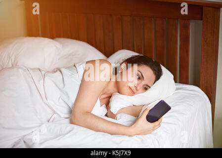 Giovane donna in camera da letto con telefono. utilizzando lo smartphone nel concetto di letto Foto Stock