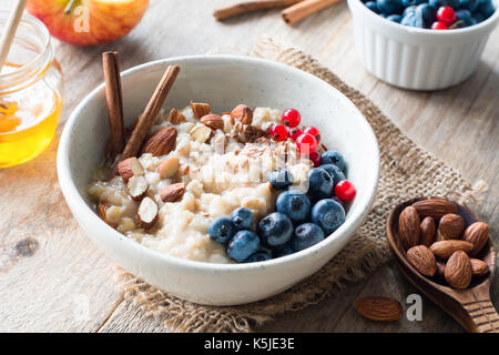 Farina di avena porridge con mirtilli, le mandorle e la cannella, il miele, i semi di lino e di ribes rosso nel recipiente. Super alimenti per una sana colazione nutriente Foto Stock