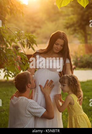Famiglia. gravidanza madre, padre e figlia. Egli bacia il ventre ritratto di famiglia al tramonto. la felicità della genitorialità Foto Stock