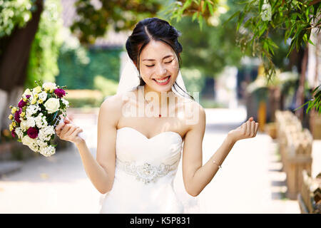 Giovane e bella sposa asiatici esultanza con bouquet in mano. Foto Stock