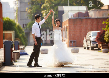 Giovani asiatici sposa e lo sposo in abito da sposa in ballo nel parcheggio. Foto Stock