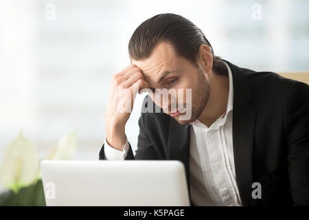 Perplesso giovane impreditore guardando lo schermo del notebook al posto di lavoro. Foto Stock