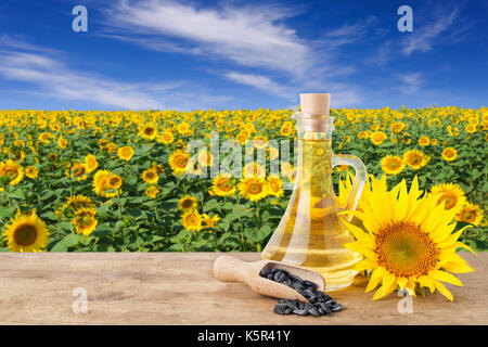 Olio di semi di girasole in una bottiglia di vetro, semi nel convogliatore, girasoli freschi sul tavolo di legno con sfondo naturale. blooming campo di girasoli con cielo blu. agric Foto Stock