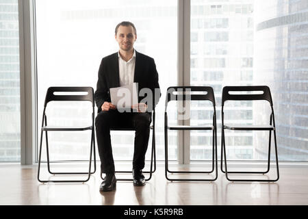 Sorridente ambizioso giovane uomo in attesa per un colloquio o un incontro. Foto Stock