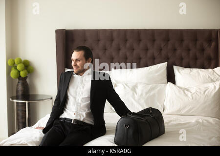 Happy businessman con bagagli seduta sul letto in camera d'albergo. Foto Stock