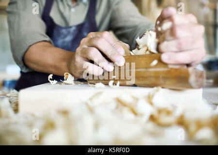 Inquadratura ravvicinata di un irriconoscibile artigiano utilizzando giuntatrice piano, trucioli in primo piano Foto Stock