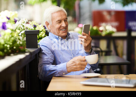 Ritratto di sorridente imprenditore senior con la video chiamata tramite smartphone in outdoor cafe lounge Foto Stock