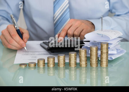 Close-up di imprenditore calcolare le fatture nella parte anteriore di una pila di monete Foto Stock