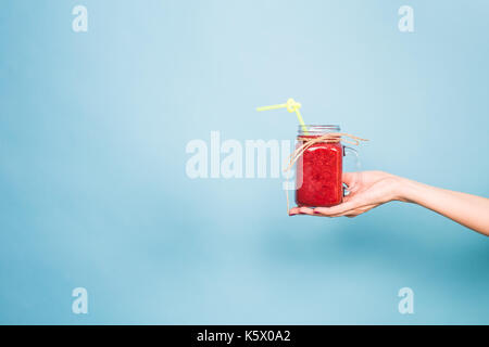 Donna di mano che trattiene il vetro di fragola e frullato rasberry su sfondo blu. Foto Stock