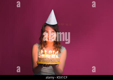 Ritratto di gioiosa ragazza con torta di compleanno e guardando la telecamera in studio Foto Stock