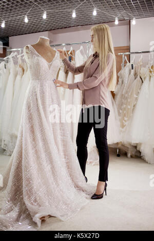 Elegante ragazza e l'abito da sposa sul manichino. Il salone. Scegliere l'abito. small business Foto Stock