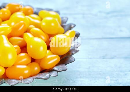 Ciotola con un mix di giallo e pera datterino cimelio di pomodori ciliegia sulla luce blu sullo sfondo di legno, foto con copia spazio. Foto Stock