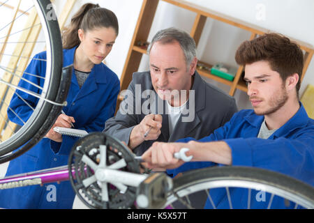 Noleggio meccanico e 2 apprendisti la riparazione di una bicicletta in officina Foto Stock