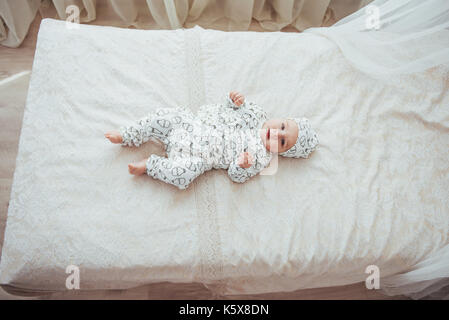 Neonato vestito con una tuta su un morbido letto in studio. Foto Stock