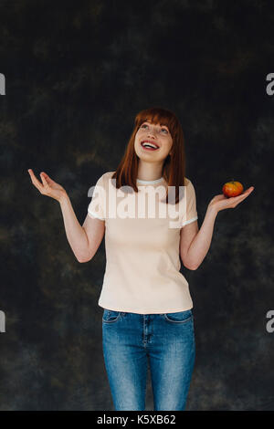 Studio shot di una donna in possesso di un Apple in una mano come si guarda in alto e mantiene il suo altro lato. Foto Stock