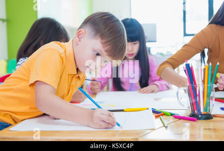 I bambini di età prescolare Disegno con matite colorate su carta bianca sulla tavola in aula con gli amici e il maestro,Kindergarten concetto di istruzione Foto Stock