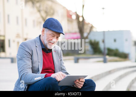 Uomo senior in città con la compressa, rendendo chiamata telefonica Foto Stock