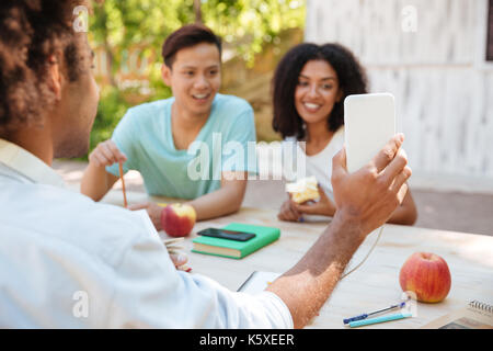 Due amici sorridenti guardando lo smartphone mentre seduti a tavola all'aperto Foto Stock