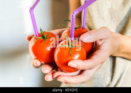 Tre mature pomodori rossi con cannucce nelle mani della donna su sfondo chiaro. succo di frutta fresco cibo sano concetto. il pomodoro in un recipiente con del succo di frutta fresco Foto Stock