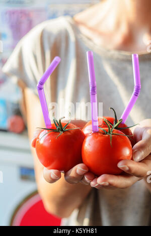 Tre mature pomodori rossi con cannucce nelle mani della donna su sfondo chiaro. succo di frutta fresco cibo sano concetto. il pomodoro in un recipiente con del succo di frutta fresco Foto Stock