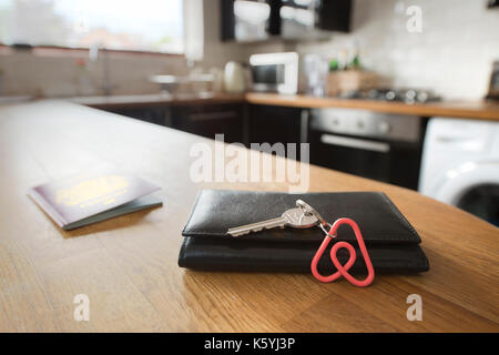 Un portachiavi Airbnb appoggia contro un portafogli nella cucina di un appartamento Airbnb disponibile a noleggio da parte degli ospiti, con un passaporto britannico dietro. Foto Stock